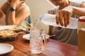 Woman pouring cold water from bottle into glass at dinner table. Royalty Free Stock Photo