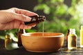 Woman pouring essential oil from glass bottle into bowl on table