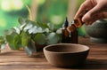 Woman pouring eucalyptus essential oil into bowl on wooden table Royalty Free Stock Photo