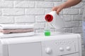 Woman pouring fabric softener from bottle into cap on washing machine near white brick wall, closeup Royalty Free Stock Photo