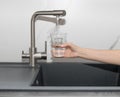 Woman pouring filtered water from tap into glass in kitchen Royalty Free Stock Photo