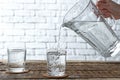 Woman pouring fresh water from jug into glass on wooden table Royalty Free Stock Photo