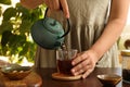 Woman pouring freshly brewed tea from teapot into cup at table indoors, closeup. Traditional ceremony