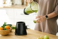 Woman pouring green smoothie to glass close-up