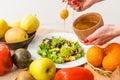 Woman pouring honey mustard dressing into bowl with fresh salad on table Royalty Free Stock Photo