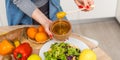 Woman pouring honey mustard dressing into bowl with fresh salad on table Royalty Free Stock Photo