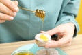 Woman pouring honey onto cookie at wooden table, closeup