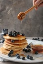 Woman pouring honey onto delicious pancakes with berries on light table Royalty Free Stock Photo