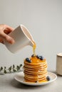 Woman pouring honey onto tasty pancakes with berries on table Royalty Free Stock Photo