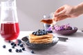 Woman pouring honey onto tasty pancakes with blueberries at light table Royalty Free Stock Photo