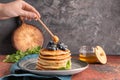 Woman pouring honey onto tasty pancakes with blueberries at table Royalty Free Stock Photo