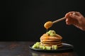 Woman pouring honey onto tasty pancakes with kiwi on dark background Royalty Free Stock Photo