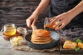 Woman pouring honey onto tasty pancakes at wooden table Royalty Free Stock Photo
