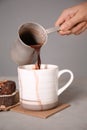 Woman pouring hot chocolate from cezve into cup on grey table Royalty Free Stock Photo