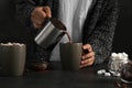 Woman pouring hot chocolate with milk into cup on table Royalty Free Stock Photo