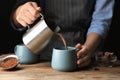 Woman pouring hot cocoa drink into cup on table, closeup Royalty Free Stock Photo