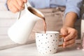 Woman pouring hot cocoa drink into cup on wooden table, closeup Royalty Free Stock Photo