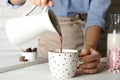 Woman pouring hot cocoa drink into cup on wooden table, closeup Royalty Free Stock Photo