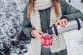 Woman pouring hot tea out of vacuum flask in snowy winter park. Cup with drink dressed in red knitted Christmas sweater Royalty Free Stock Photo