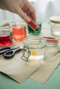 Woman pouring liquid orange Easter cold colour color in glass with water and vinegar next to green, yellow, red, blue dye in Royalty Free Stock Photo