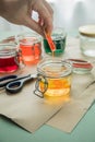 Woman pouring liquid orange Easter cold colour color in glass with water and vinegar next to green, yellow, red, blue dye in Royalty Free Stock Photo