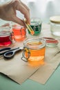 Woman pouring liquid orange Easter cold colour color in glass with water and vinegar next to green, yellow, red, blue dye in Royalty Free Stock Photo