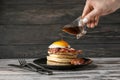 Woman pouring maple syrup onto tasty pancakes with fried egg and bacon