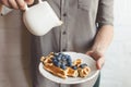 Woman pouring maple syrup on tasty waffles