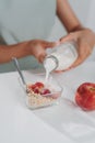 Woman pouring milk from bottle into bowl with corn flakes on table in kitchen Royalty Free Stock Photo