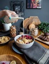 Woman pouring milk into the bowl with granola, bananas, nuts, and berries for breakfast Royalty Free Stock Photo