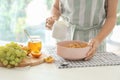 Woman pouring milk into bowl from jug with corn flakes at table Royalty Free Stock Photo