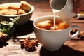Woman pouring milk into cup of anise tea at wooden table, closeup. Space for text Royalty Free Stock Photo