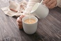 Woman pouring milk into cup of tea on table Royalty Free Stock Photo