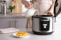 Woman pouring milk into modern multi cooker for making delicious yogurt at table