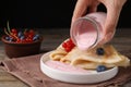 Woman pouring natural yogurt onto crepes with blueberries and red currants at wooden table, closeup Royalty Free Stock Photo