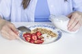 Woman pouring plant based milk into homemade granola with fresh organic strawberries and yogurt in the vintage plate.