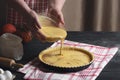Woman pouring pumpkin pie filling from a bowl into a tray, on a black rustic table, surrounded by ingredients. Home cooking