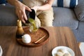 Woman pouring ready matcha green tea drink at home using tea ceremony set