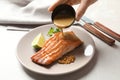 Woman pouring sauce onto tasty cooked salmon