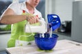 A woman is pouring some powder into a bowl of dough and uses a s Royalty Free Stock Photo