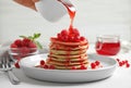 Woman pouring syrup onto fresh pancakes with berries on white table