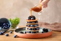 Woman pouring syrup onto tasty pancakes with berries on plate Royalty Free Stock Photo