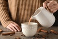 Woman pouring tasty cocoa from jug into cup on wooden table Royalty Free Stock Photo