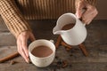 Woman pouring tasty cocoa from jug into cup on wooden table Royalty Free Stock Photo