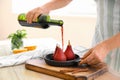 Woman pouring wine onto pan with sweet pears in kitchen