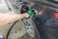 Woman pours fuel into the tank of a black car on gasoline station. Transportation concept.