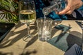 A woman pours water into a glass next to a glass of white wine i