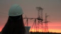 A woman power engineer in white helmet inspects power line using data from electrical sensors on a tablet. High voltage