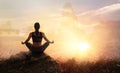 Woman practices meditating yoga at is an asana on a stone, sunset mountains background
