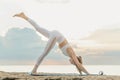 Woman practices yoga downward facing dog with one leg up on the beach. Caucasian girl doing exercise at seashore Royalty Free Stock Photo